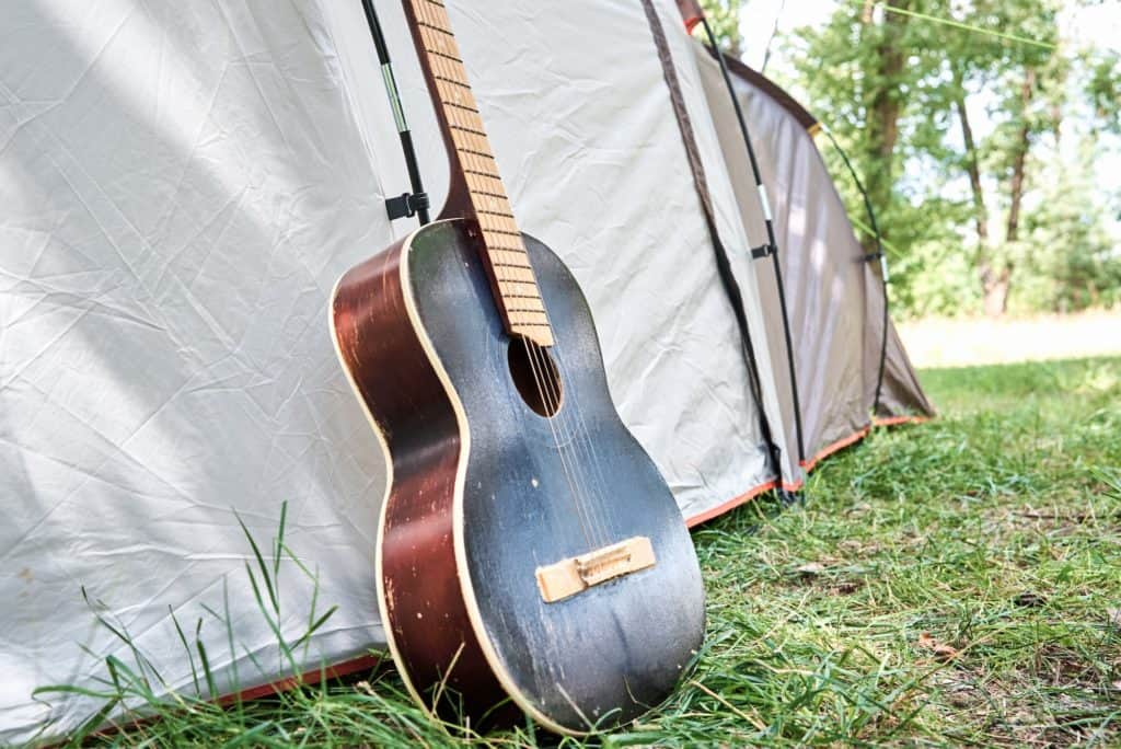 Guitarra acústica perto de uma barraca de acampamento na floresta