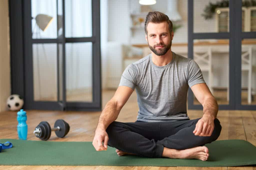 Przystojny młody mężczyzna siedzi na macie do jogi w domu