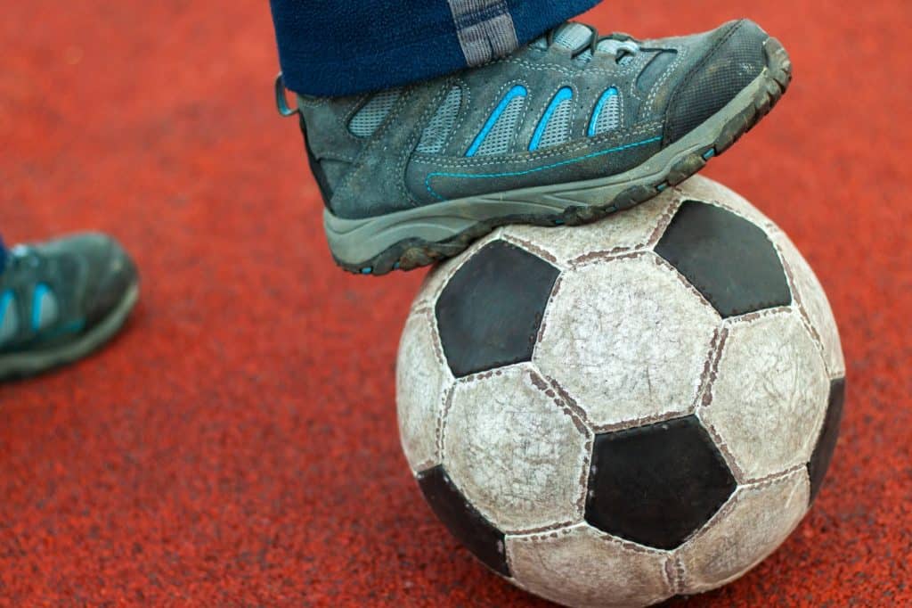 Piede umano in una scarpa da ginnastica sporca su un vecchio pallone da calcio