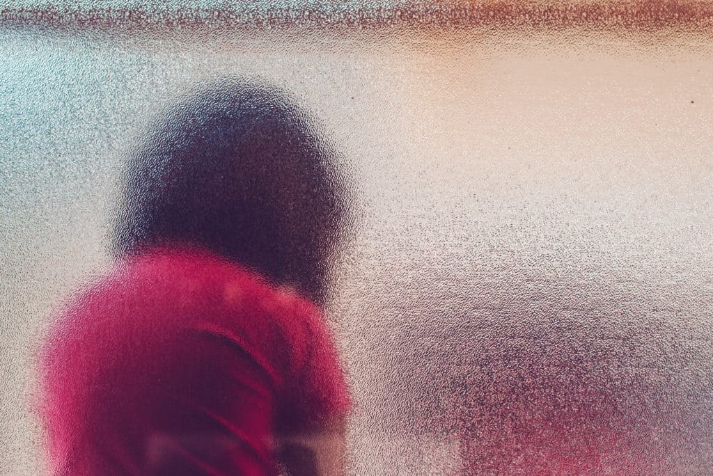 Schattenbild eines nicht erkennbaren traurigen autistischen Mädchens hinter beflecktem gl