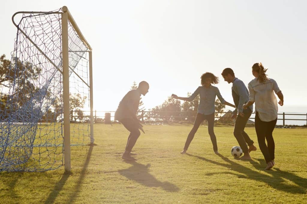 Jovens adultos jogando futebol no parque um no gol, vista lateral